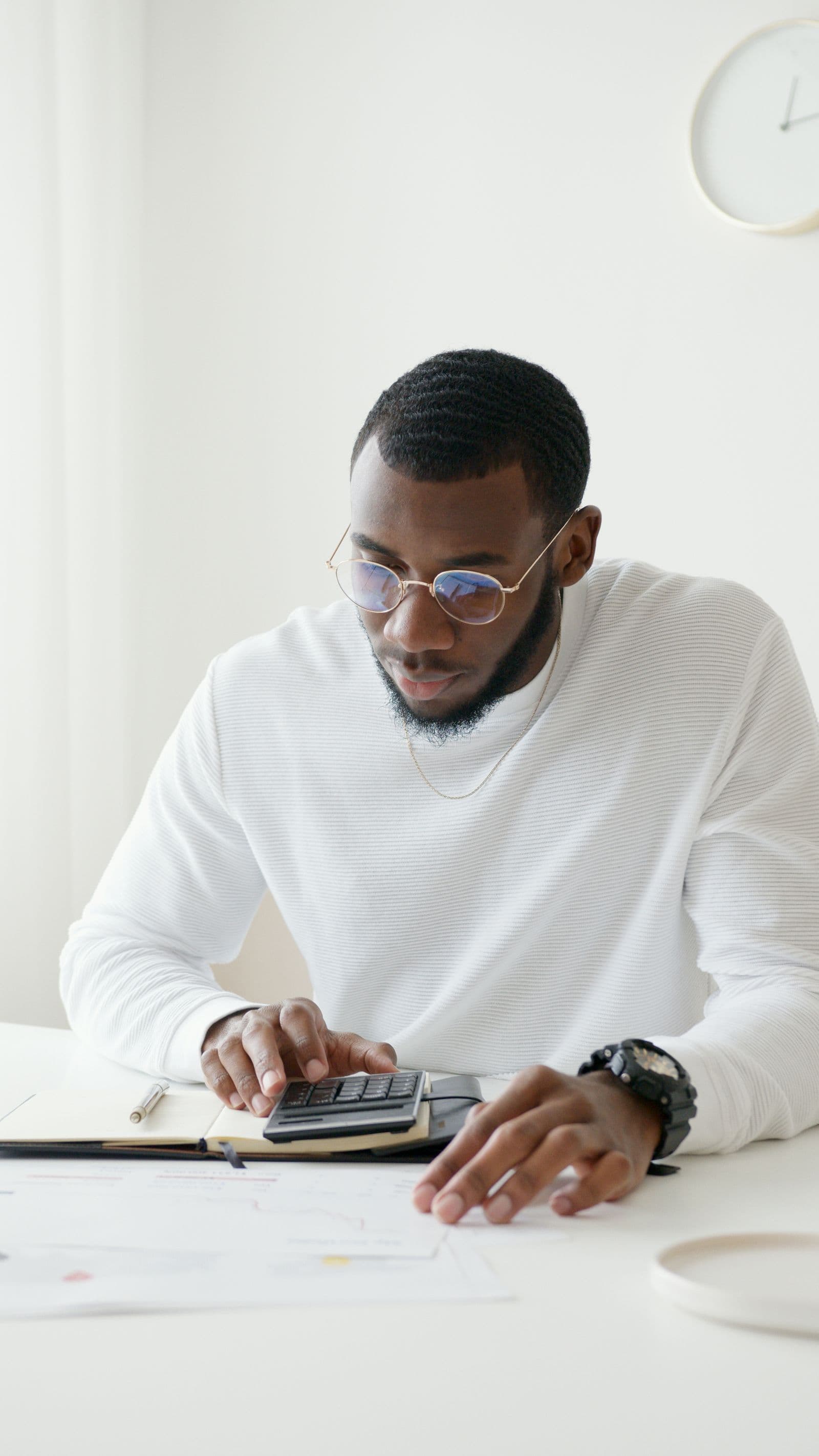 A man in glasses working through numbers on a calculator at his desk