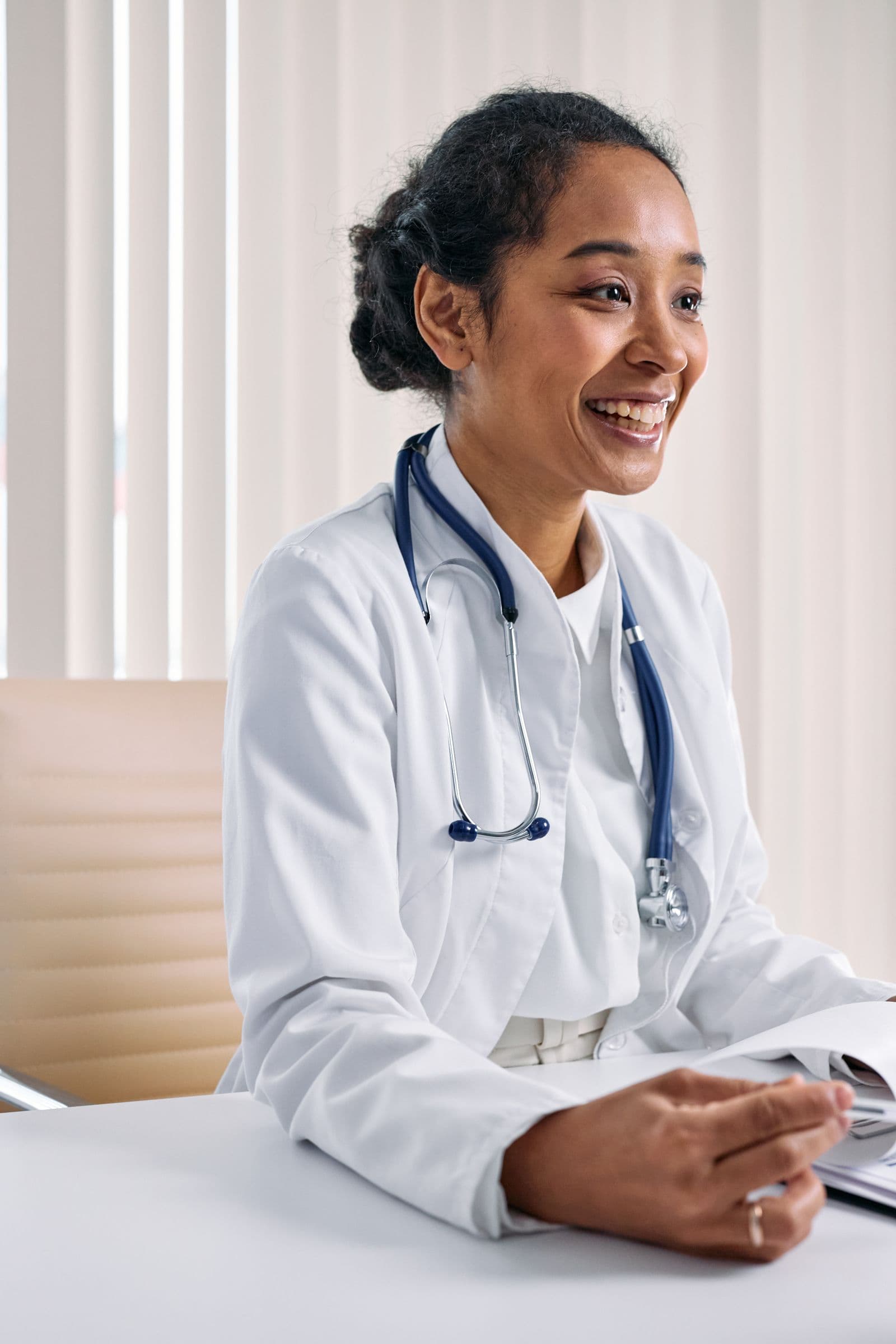 A smiling doctor in a white coat sitting at her consulting desk