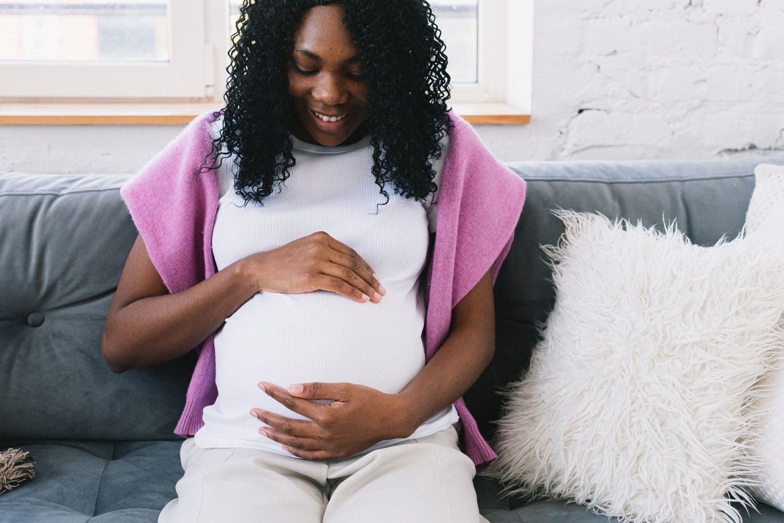 A smiling pregnant woman sitting on a sofa with her hands on her belly