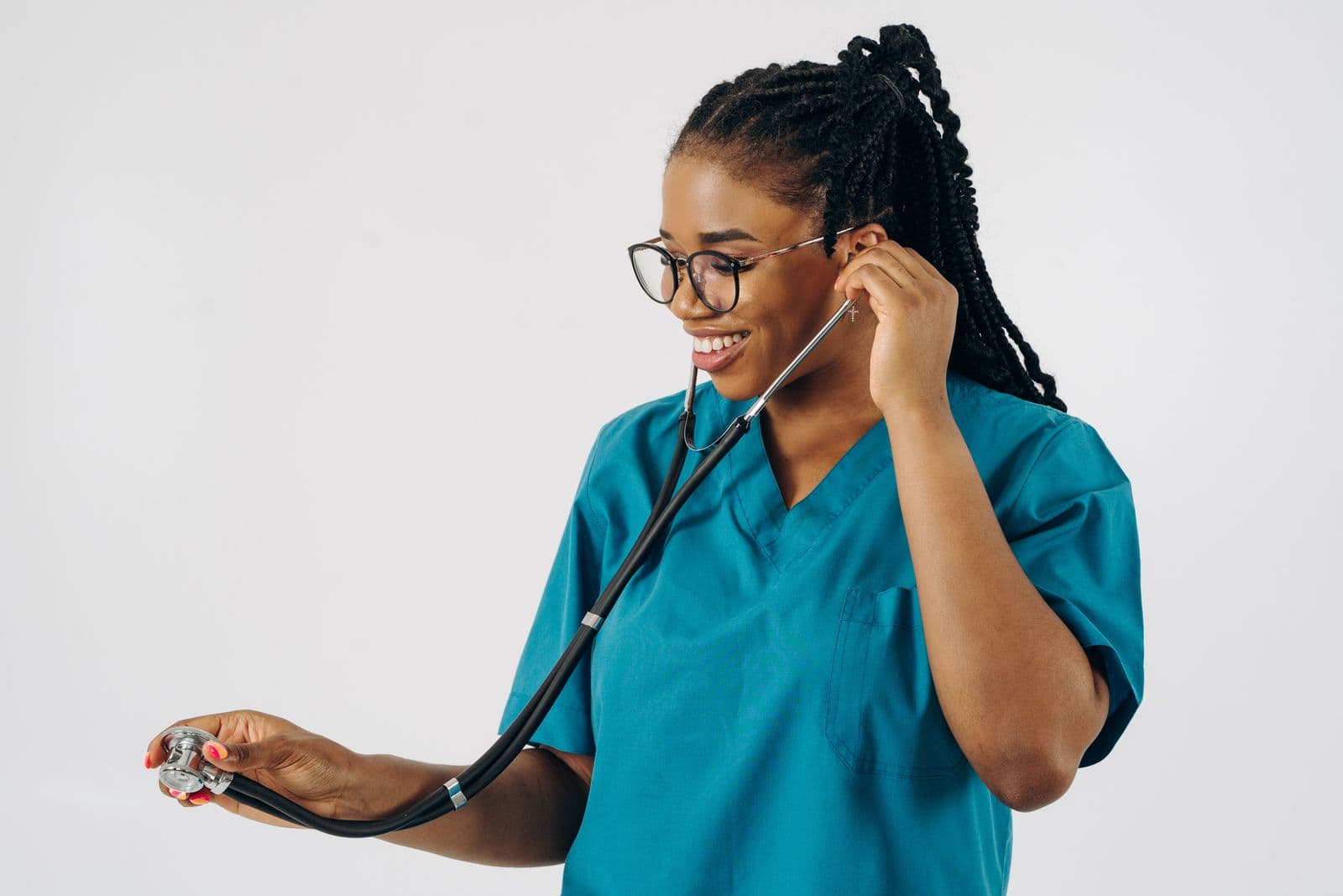 A doctor in scrubs holding a stethoscope and smiling