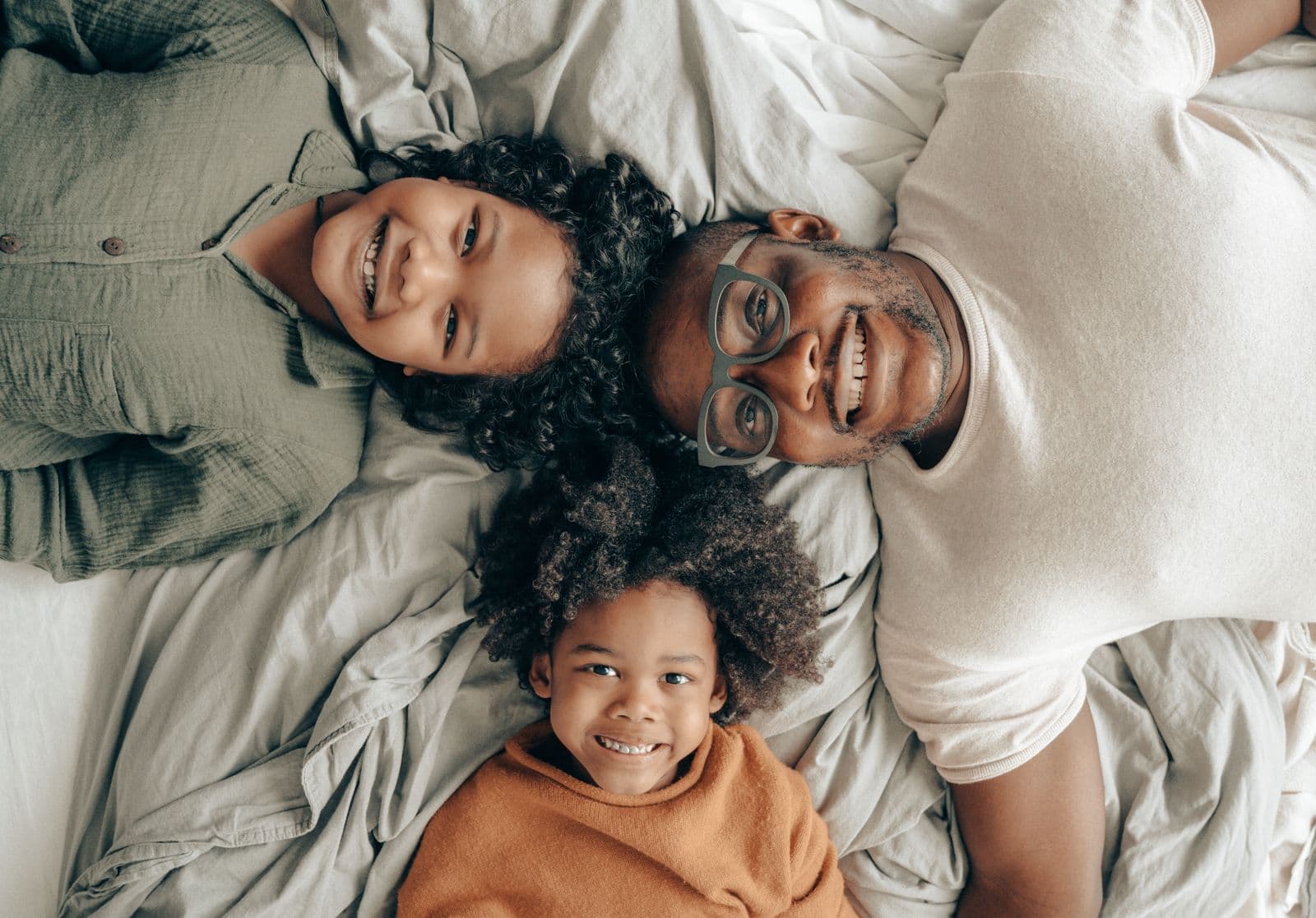 A smiling father, mother and child lying together on a bed