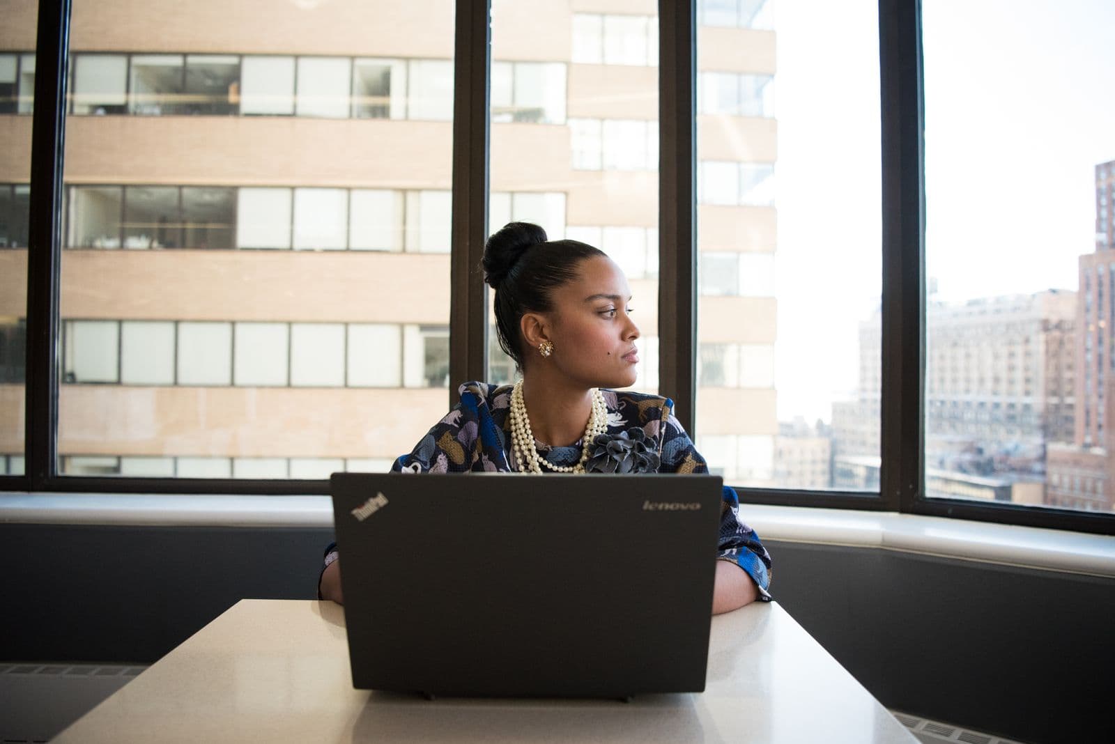 A woman at a laptop in a bright office, looking out of the window